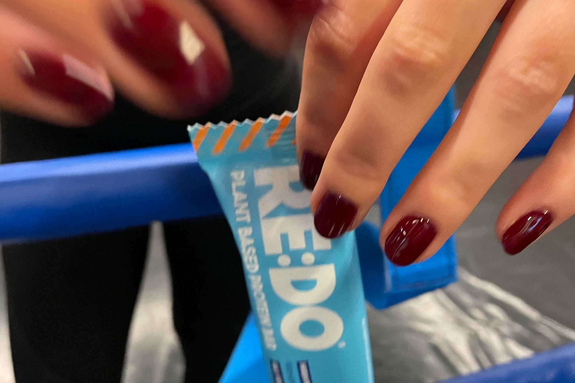 A hand with red nails holding a RE:DO bar